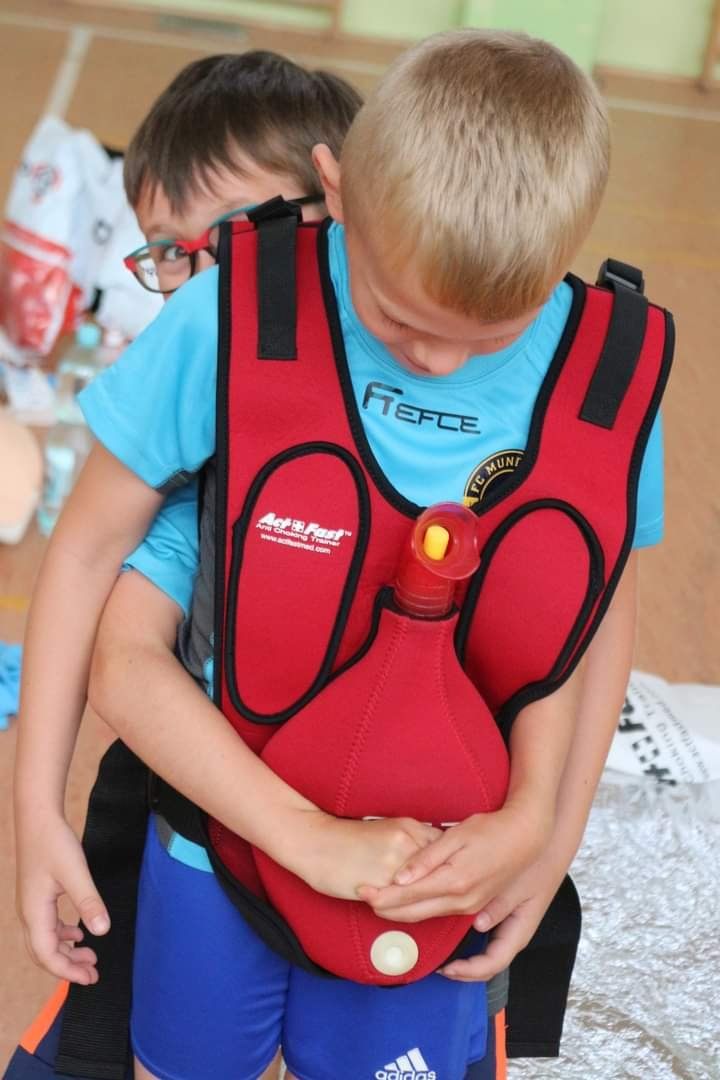 Dziecko ćwiczy pierwszą pomoc w kamizelce treningowej do nauki postępowania przy zadławieniu